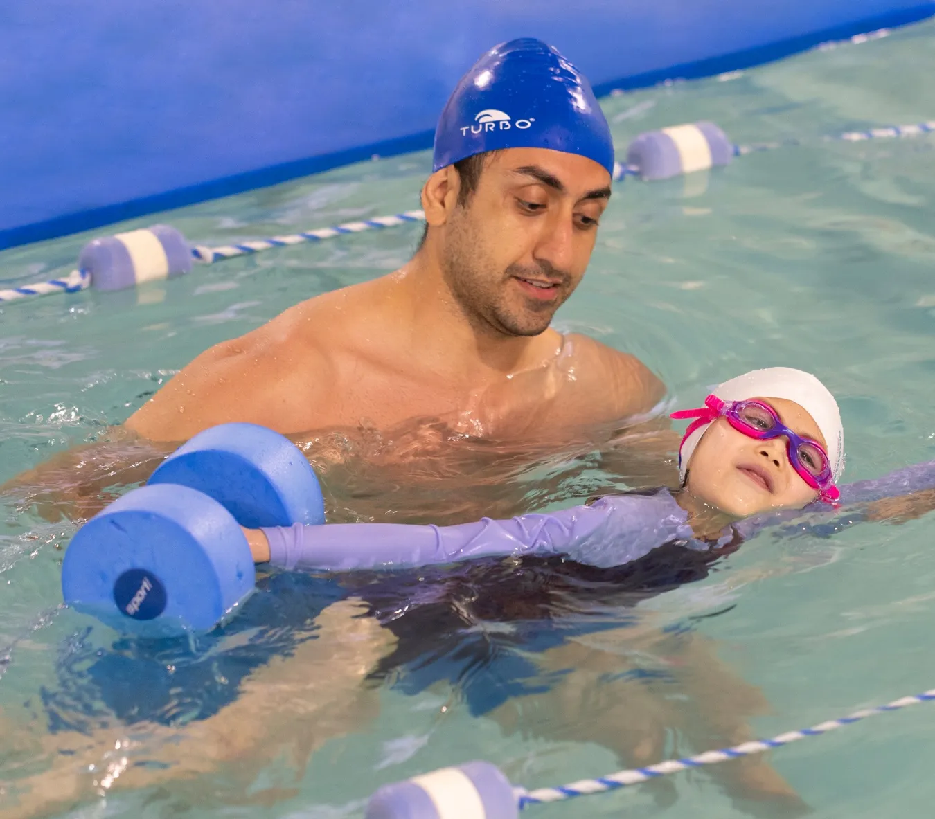 Marina’s Swim School instructor guiding a young swimmer using water dumbbells to practice floating and balance.