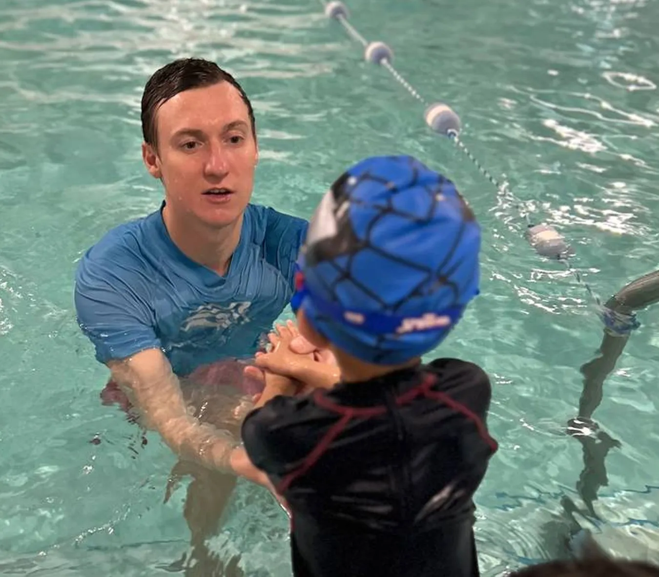 Marina’s Swim School instructor guiding a young swimmer through a gliding exercise in a warm indoor pool.
