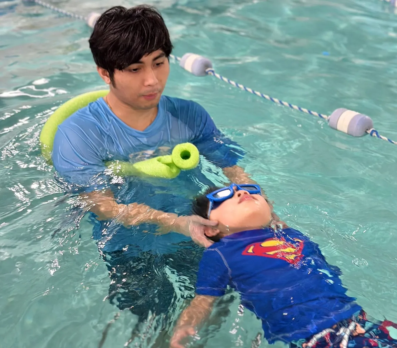 Marina’s Swim School instructor teaching a young swimmer to float and swim on their back in a warm indoor pool.