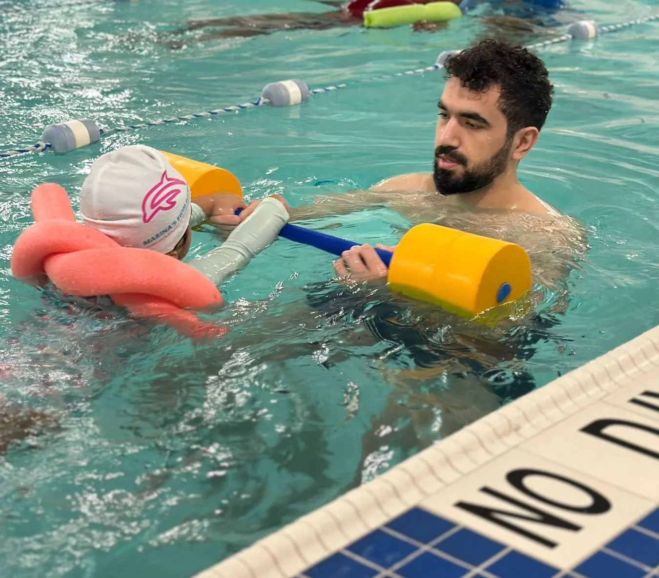 Marina’s Swim School instructor teaching a young swimmer proper kicking technique in a warm indoor pool.