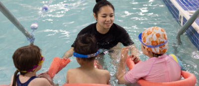 Marina’s Swim School instructor teaching a small group of young swimmers using pool noodles in a warm indoor pool.