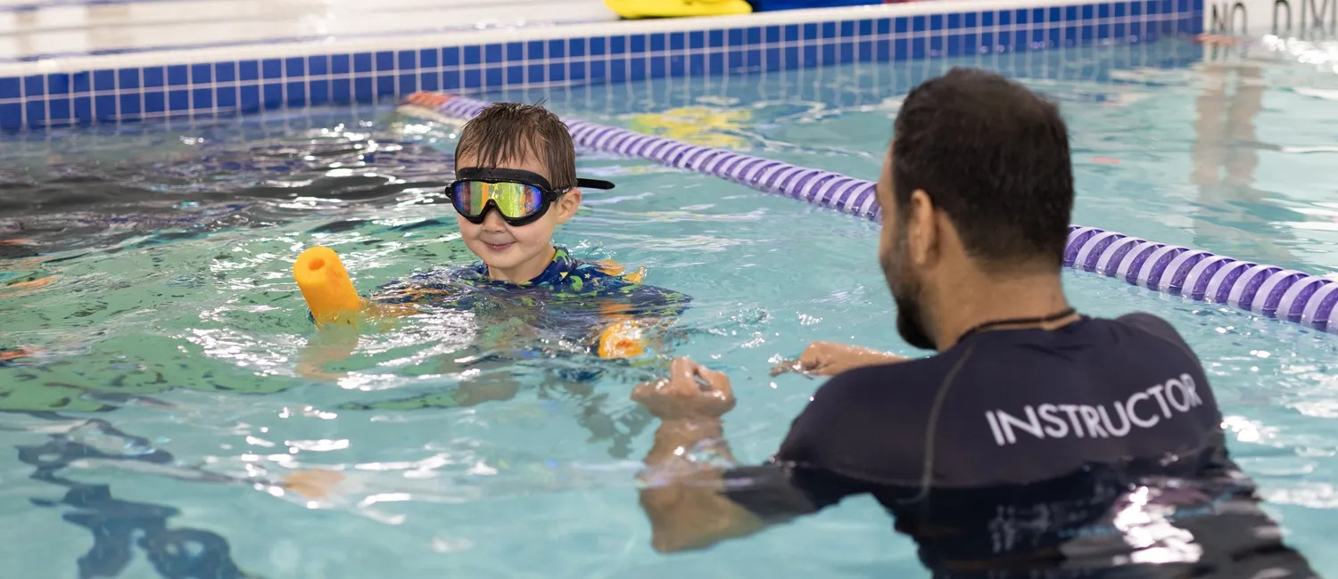 Swim instructor teaching a young student with goggles and a pool noodle at Marina’s Swim School.