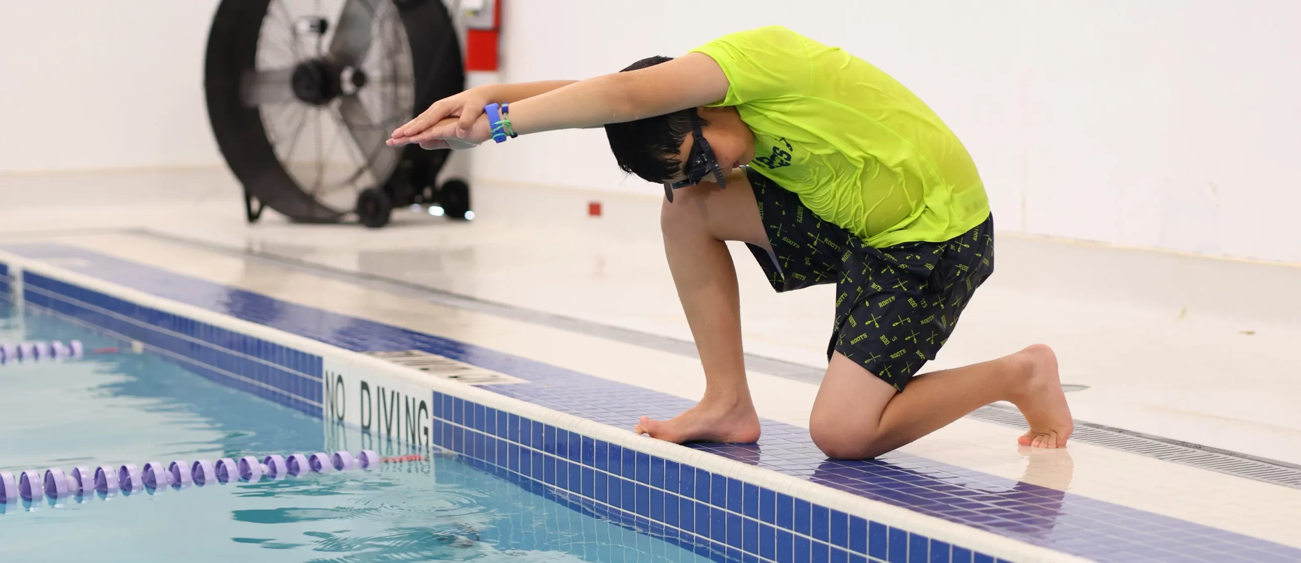 Young swimmer preparing to dive at the edge of the pool during a lesson at Marina’s Swim School.