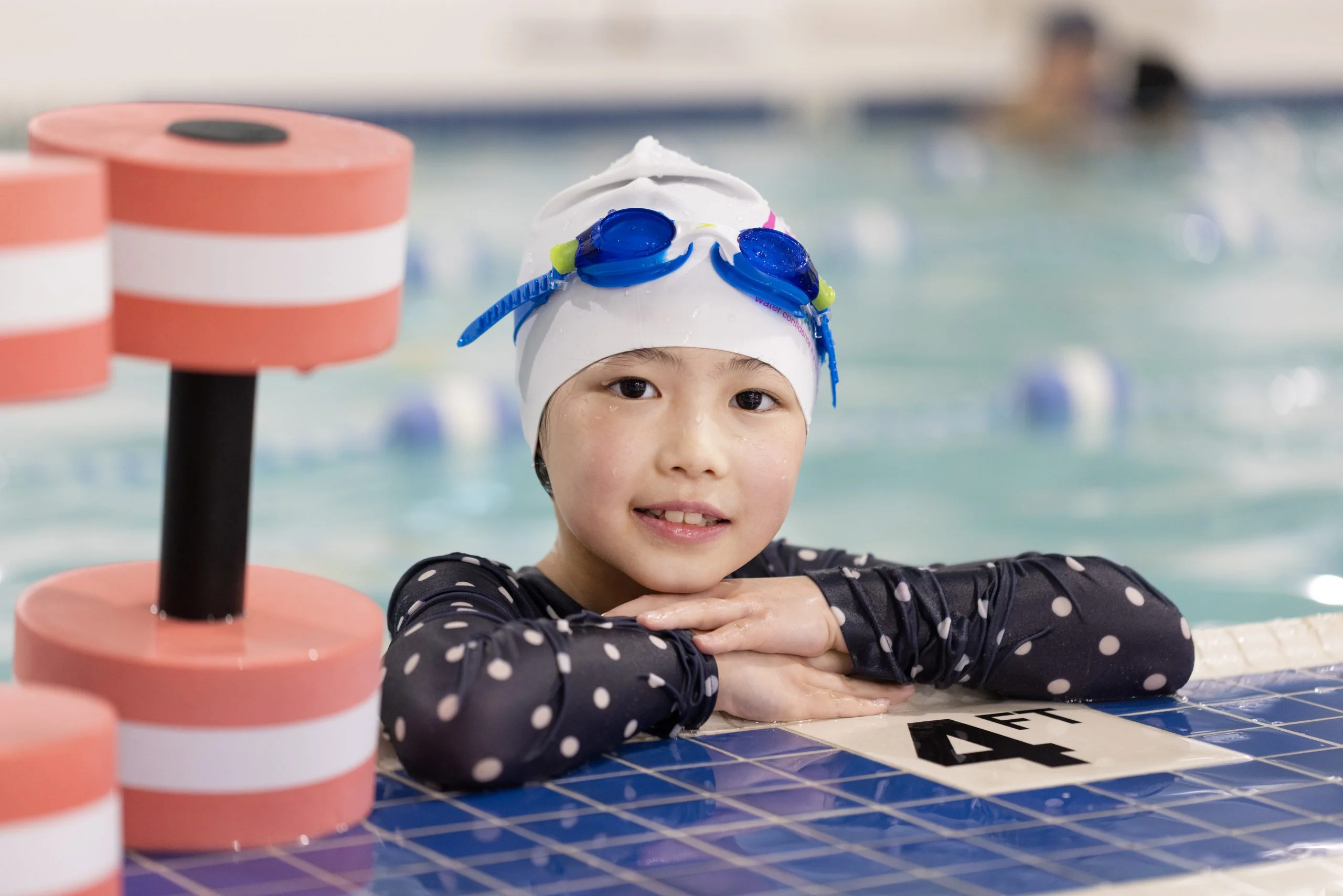 "Young swimmer wearing goggles and a swim cap resting at the pool edge during a lesson at Marina Swim School."